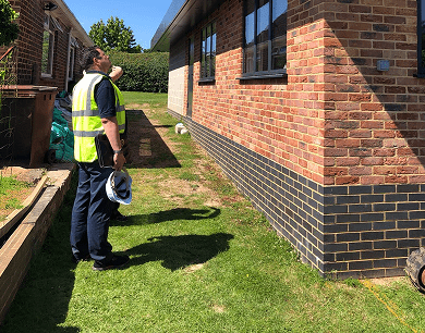 A man wearing a hi-vis vest inspecting a brick house